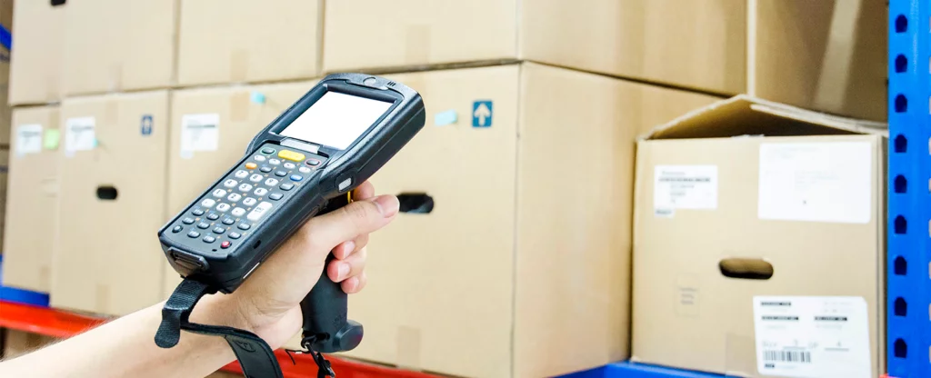 Handheld device with Windows CE held by a person scanning packages in a warehouse.
